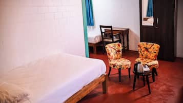 Una habitación con una cama individual, dos sillones con estampado floral, un escritorio de madera y una puerta oscura.