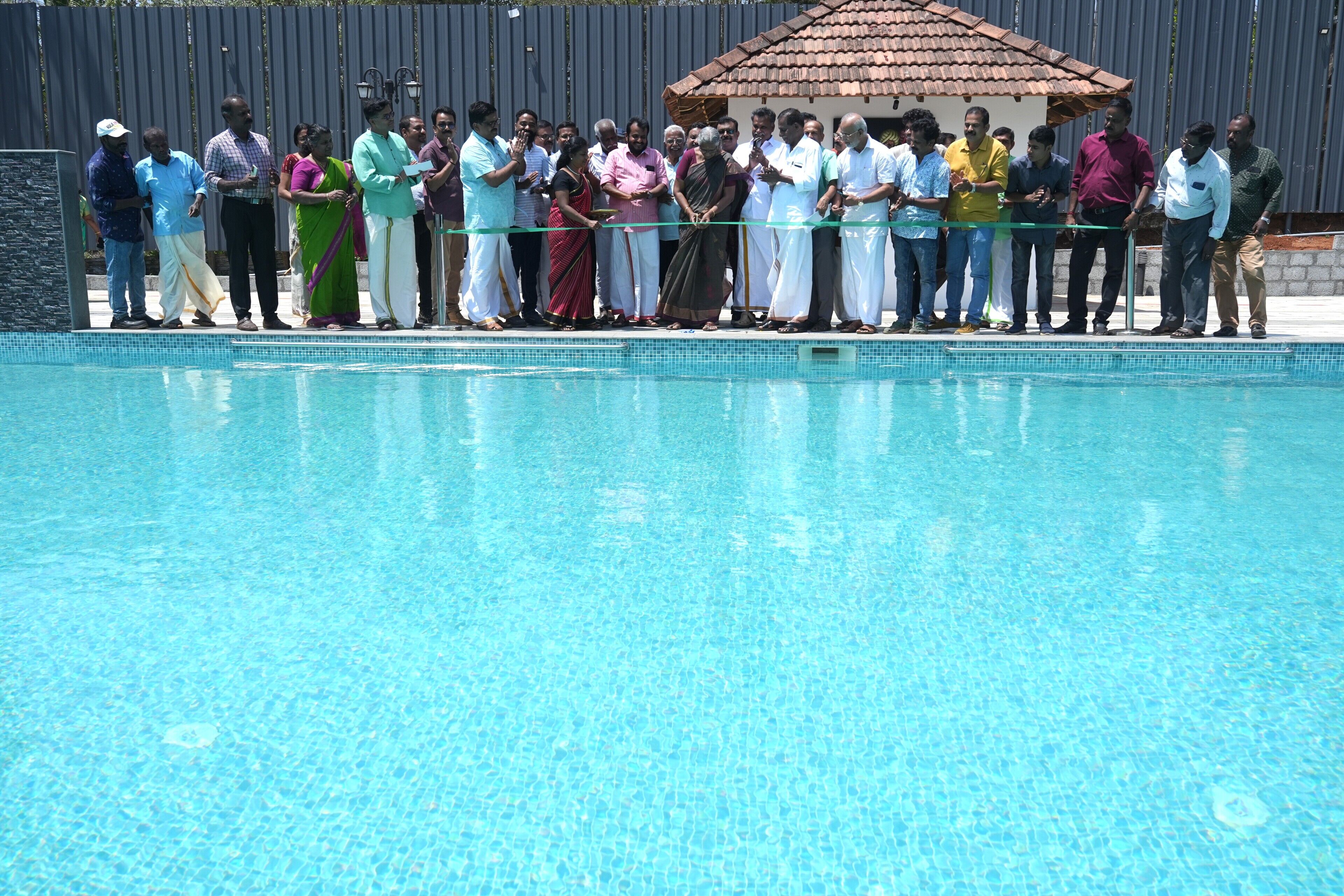 A group of people standing by a swimming pool, with a tiled roof structure in the background.