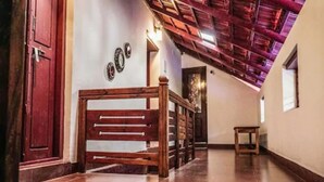 A hallway with a wooden bench, a red door, and a ceiling with exposed beams. - Anamala Serenity Homestay (Talappilly)