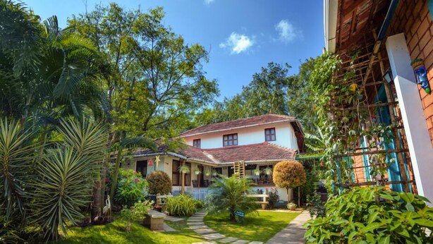 A house with a tiled roof, surrounded by lush greenery and a stone pathway leading to the entrance. - Anamala Serenity Homestay (Talappilly)