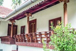 A traditional building with a wooden balcony, a tiled roof, and a small garden area. - Anamala Serenity Homestay (Talappilly)