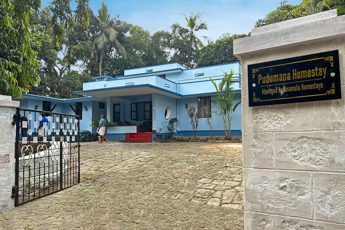 A two-story blue house with a sign indicating it is a homestay managed by Anamal Homestays.