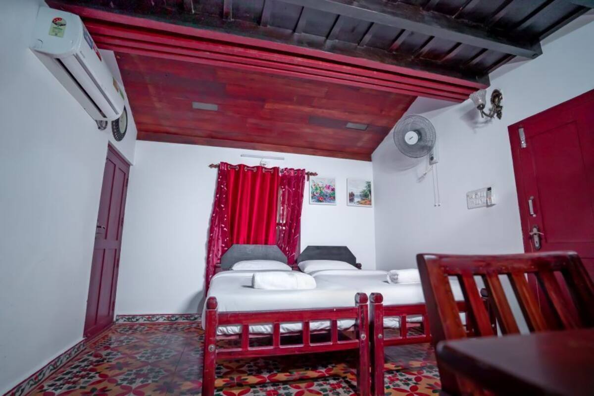 A room with a bed, a chair, a fan, and a red door.