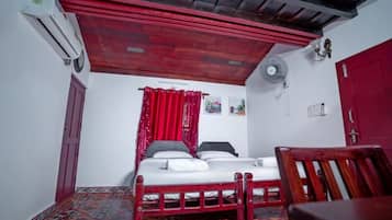 Una habitación con una cama, una silla, un ventilador y una puerta roja.