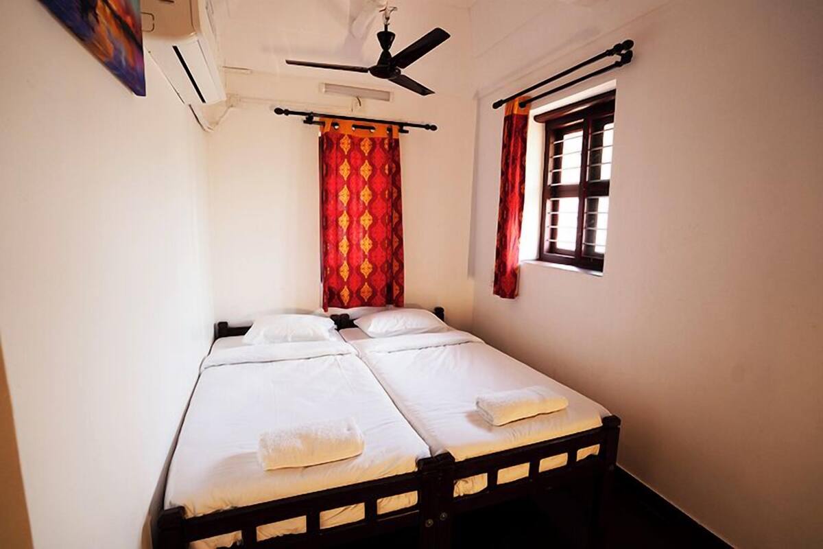 A single bed with white linens and towels, a ceiling fan, a window with curtains, and an air conditioning unit.
