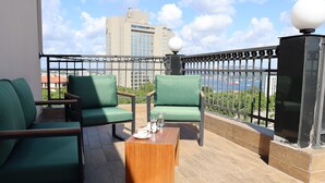 Un balcon avec des chaises vertes, une table en bois et une vue sur le paysage urbain et l’eau.