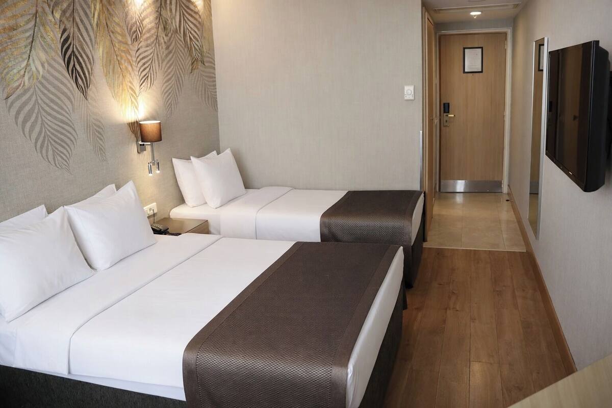 A hotel room with two beds, a wall-mounted TV, and a hallway leading to a door.