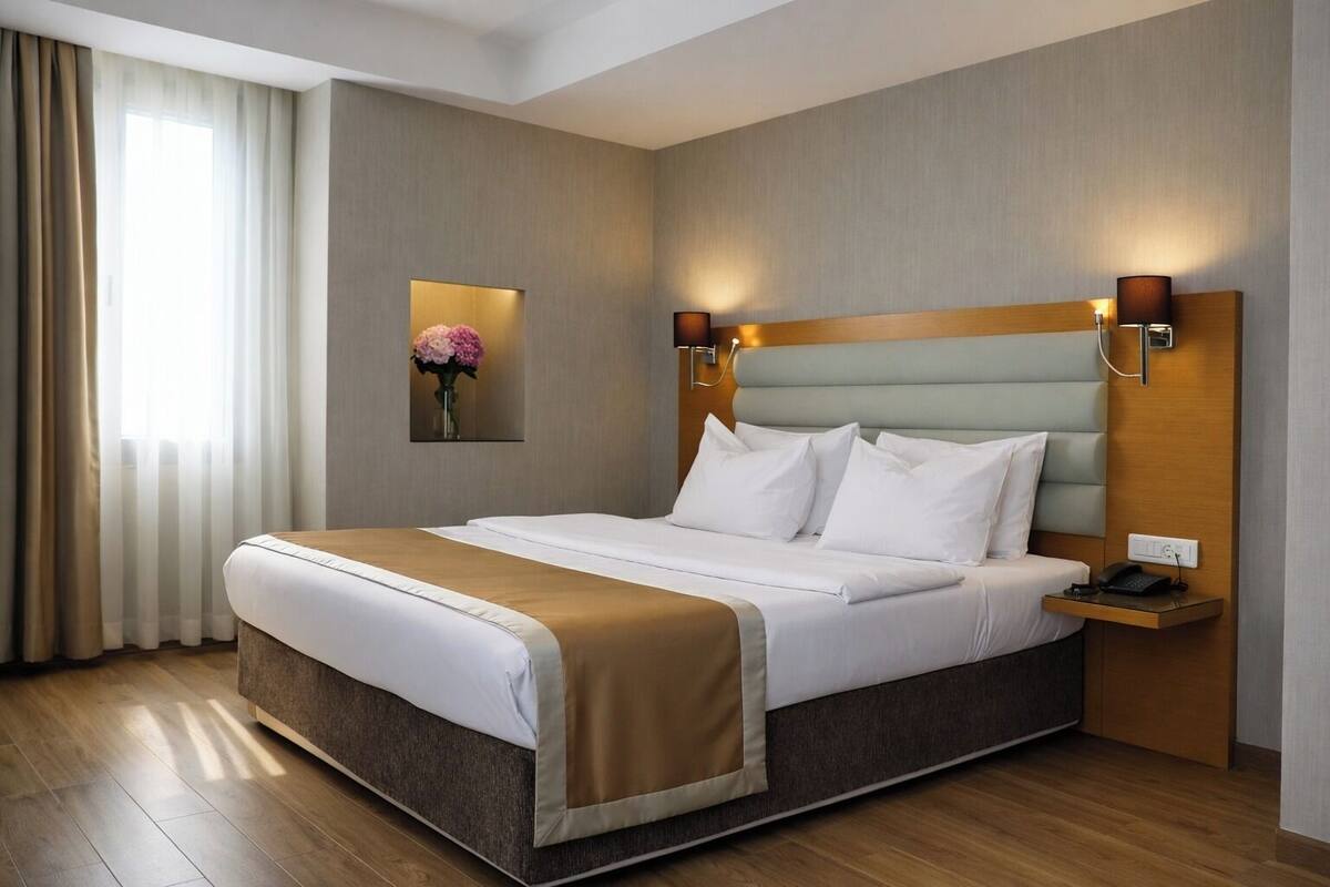A hotel room with a large bed, a bedside table with a lamp, a wall-mounted artwork, and a window with curtains.