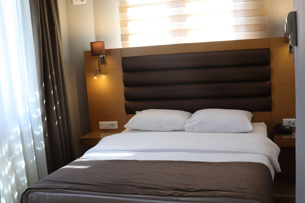 A hotel room with a large bed, a bedside table, a lamp, and a window with curtains.