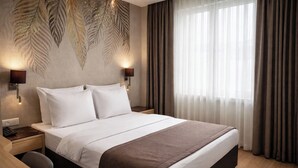 Une chambre d’hôtel avec un grand lit, deux tables de chevet, une petite table, un bureau et une chaise.