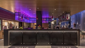 A hotel reception area with a modern design, featuring a reception desk, a bar area with shelves of bottles, and a large decorative sculpture. - Moxy Southampton (Southampton)