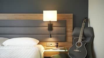 A hotel room with a bed, a nightstand with a lamp, a guitar, and a cup of coffee.