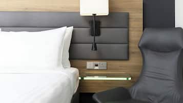 Una habitación de hotel moderna con cabecera de madera, una mesita de noche con lámpara, una silla y un enchufe.