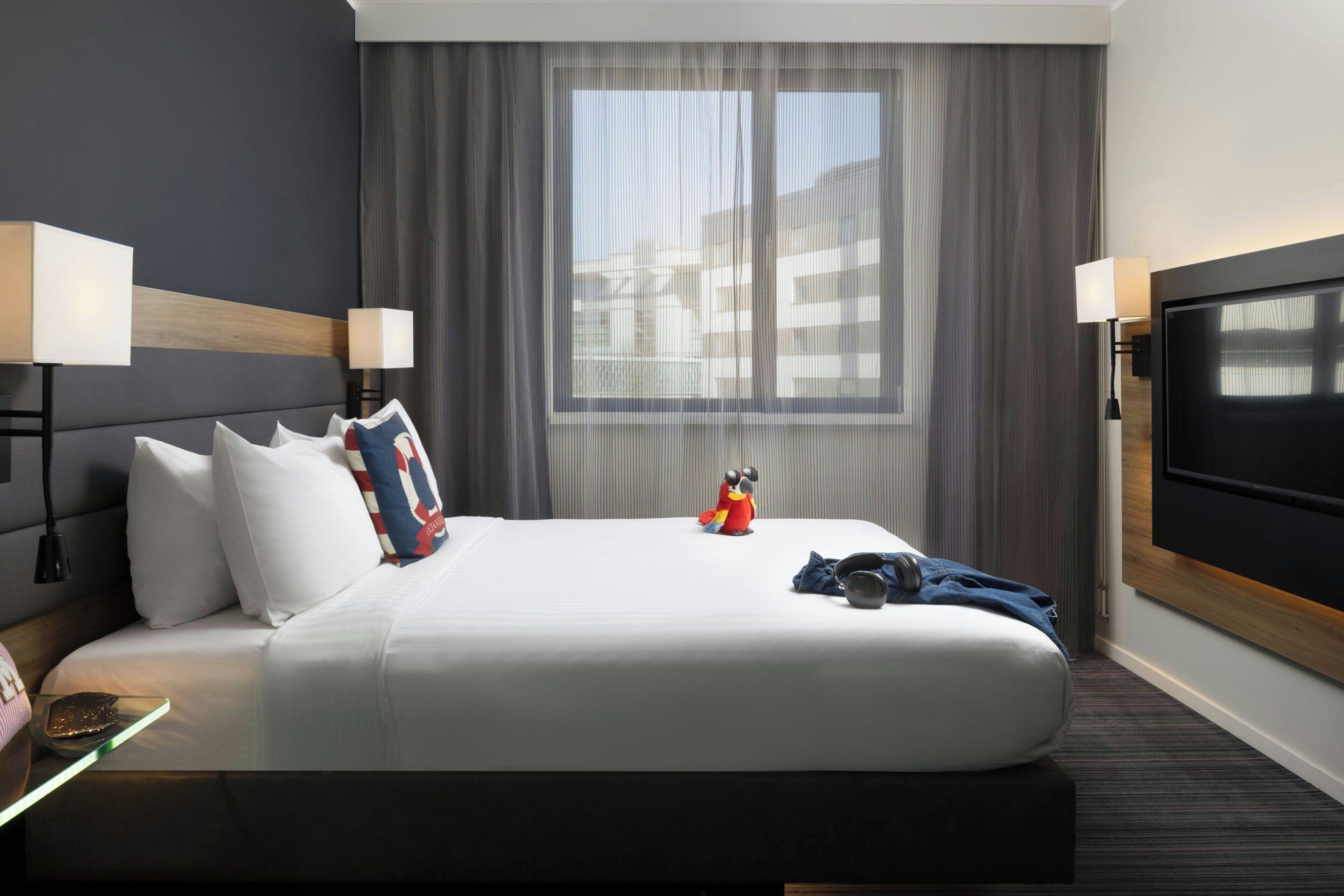 A hotel room with a large bed, two bedside lamps, a TV, and a window with curtains.