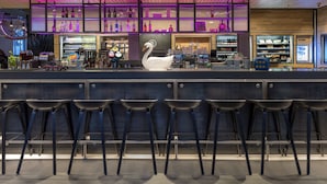 A bar area with a swan decoration, bar stools, shelves with bottles, and a neon sign. - Moxy Southampton (Southampton)