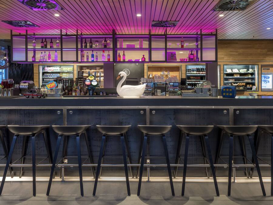A bar area with a swan decoration, bar stools, shelves with bottles, and a neon sign.
