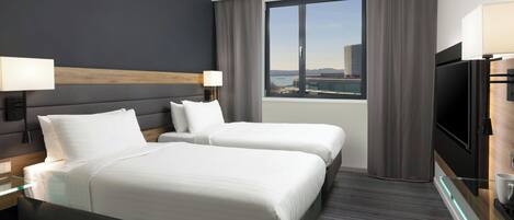 A modern hotel room with two beds, a large window with a city view, a flat-screen TV, and a red accent wall.