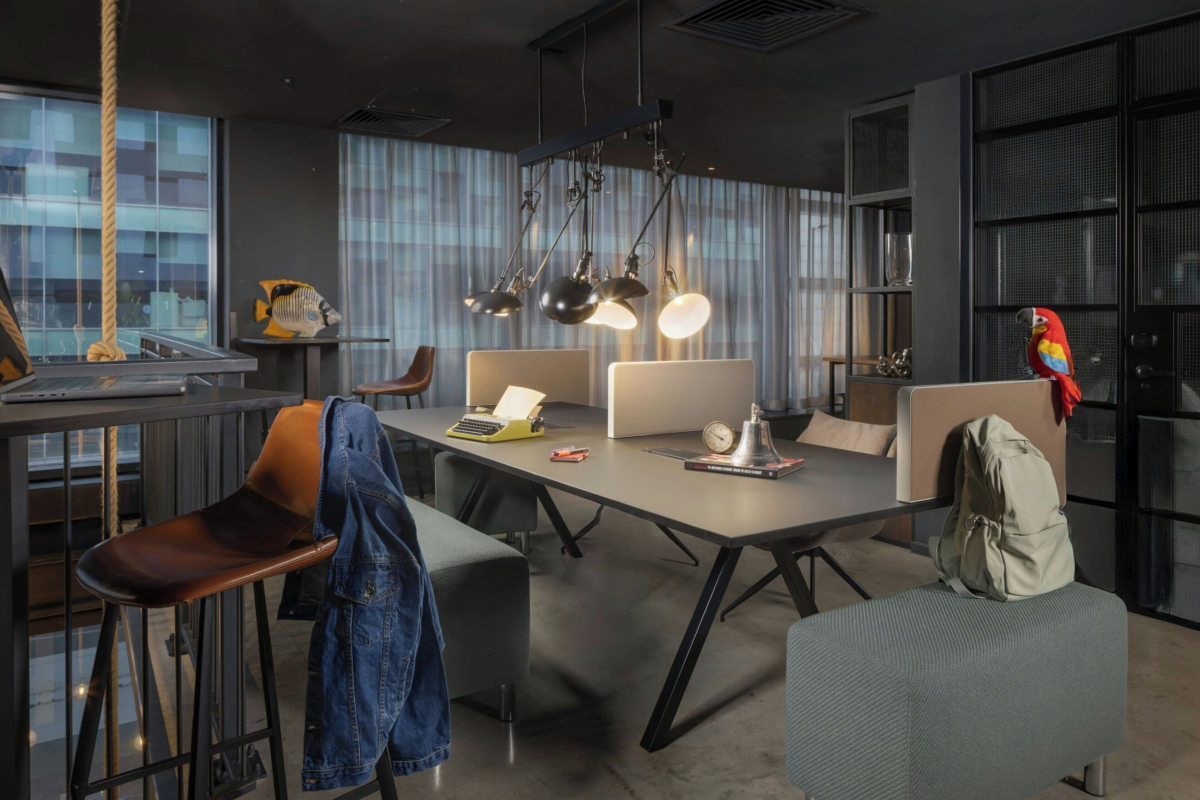 A modern office space with a long table, multiple chairs, a laptop, a typewriter, and a parrot.