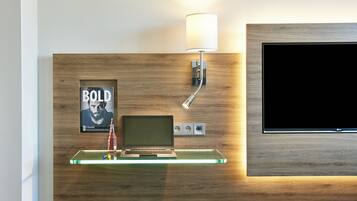 A modern room with a wooden wall, a mounted TV, a laptop, a lamp, and a framed poster.