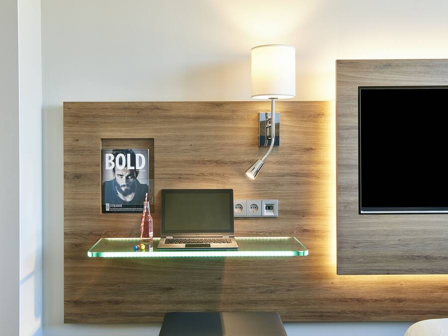 A modern room with a wooden wall, a mounted TV, a laptop, a lamp, and a framed poster.