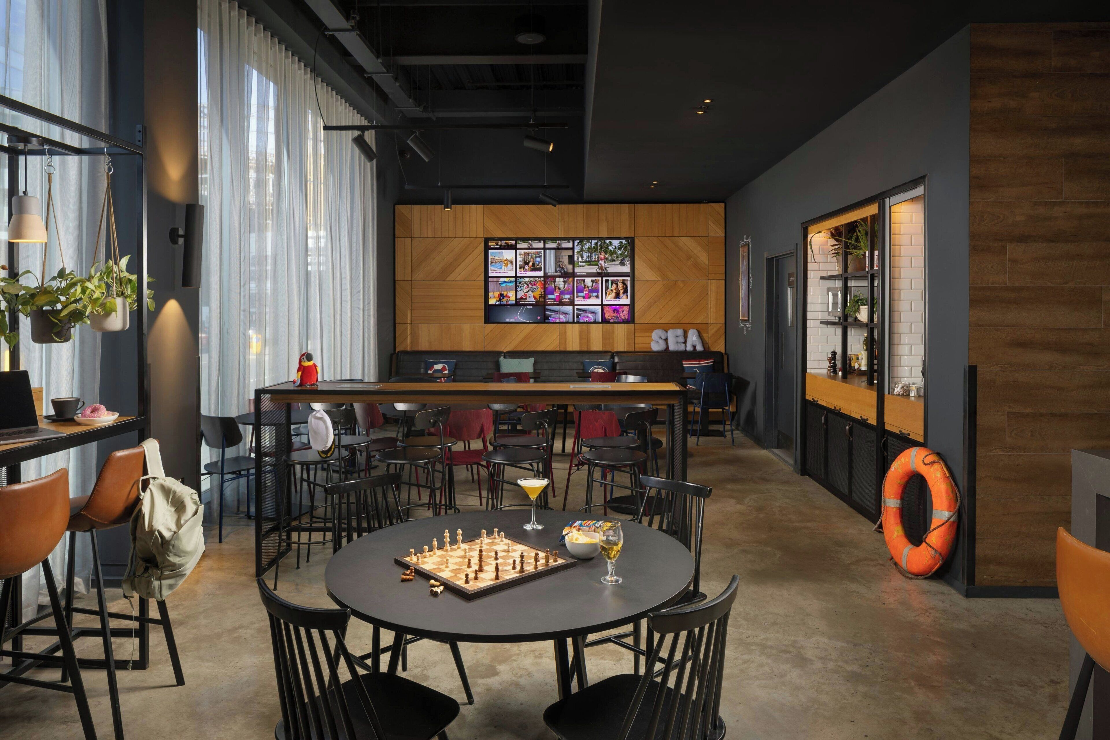 A modern bar area with a chessboard, a cocktail, and a large screen displaying images.