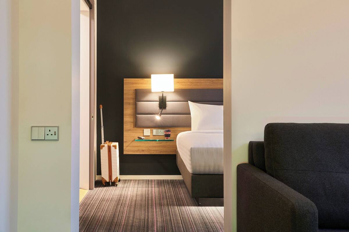 A hotel room with a bed, a bedside table with a lamp, a chair, and a radiator.