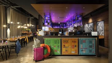A modern bar area with a long counter, multiple screens, and a staircase with purple lighting.