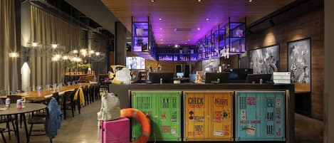 A modern bar area with a long counter, multiple screens, and a staircase with purple lighting.