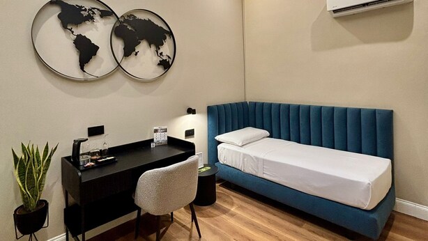 A modern bedroom with a blue bed, a desk with a chair, a world map artwork, an air conditioner, and a skylight. - Nova Relais (Naples)