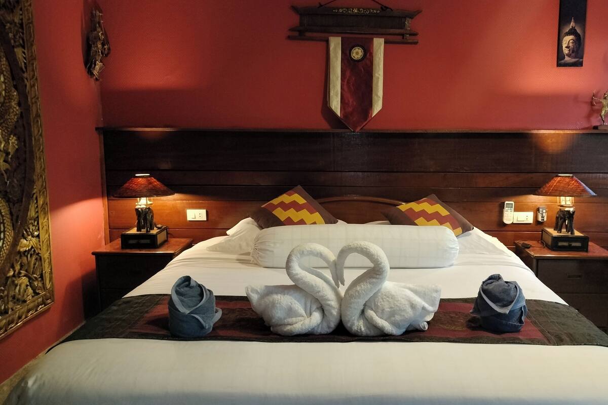 A neatly made bed with white linens, two decorative swans, and a red wall with a crest above it.