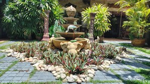 A garden with a fountain, potted plants, and a stone sculpture. - Le Prive Resort (Pattaya)