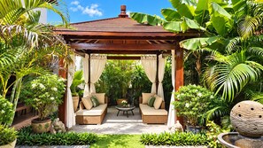 Un espace extérieur aménagé, abrité et doté de deux canapés et d’une table, entouré d’une végétation tropicale luxuriante et agrémenté d’un kiosque.