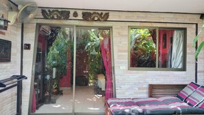 A room with a sliding glass door leading to a garden, a bed with patterned bedding, and a decorative wall piece above the door. - Le Prive Resort (Pattaya)