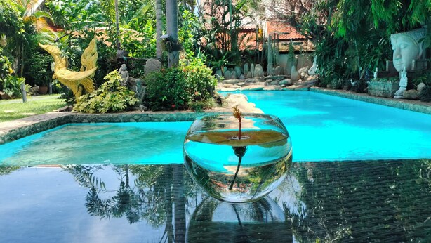 A clear glass bowl filled with water, reflecting a statue and a pool. - Le Prive Resort (Pattaya)