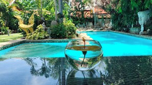 Un bol en verre transparent rempli d’eau, dans lequel se reflètent une statue et une piscine.
