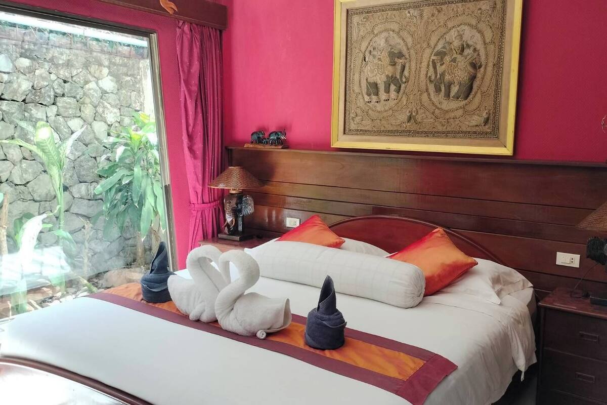 A hotel room with a bed, pillows, a nightstand, a lamp, a framed picture, and a stone wall.