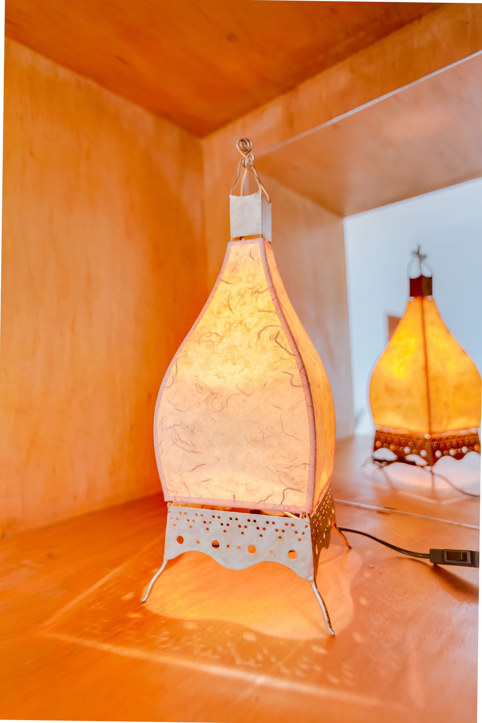 Une lampe en forme de bougie allumée, posée sur une étagère en bois.