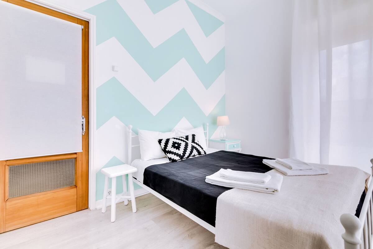 A bedroom with a bed, bedside table, and a window with curtains.