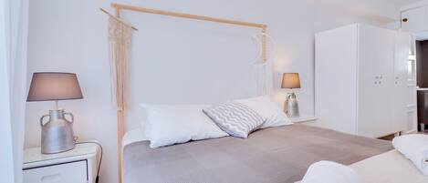 A modern bedroom with a four-poster bed, bedside tables with lamps, a wardrobe, and a macrame wall hanging.