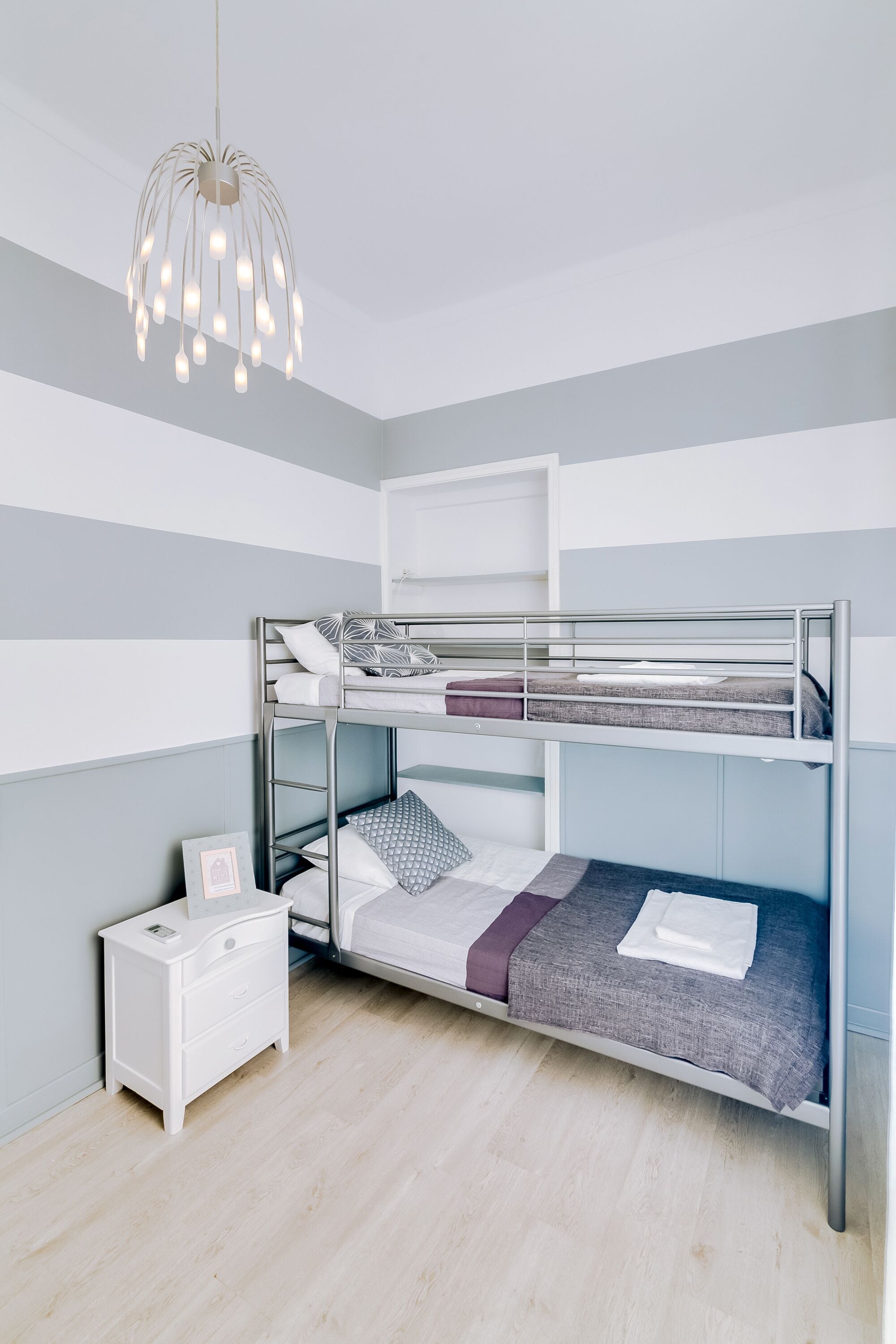 Une chambre avec un lit superposé, un luminaire suspendu, une table de chevet blanche et un tableau encadré.