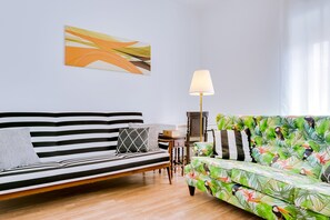 Un salon avec un canapé à rayures, un canapé à motifs floraux, une lampe et un tableau au mur.