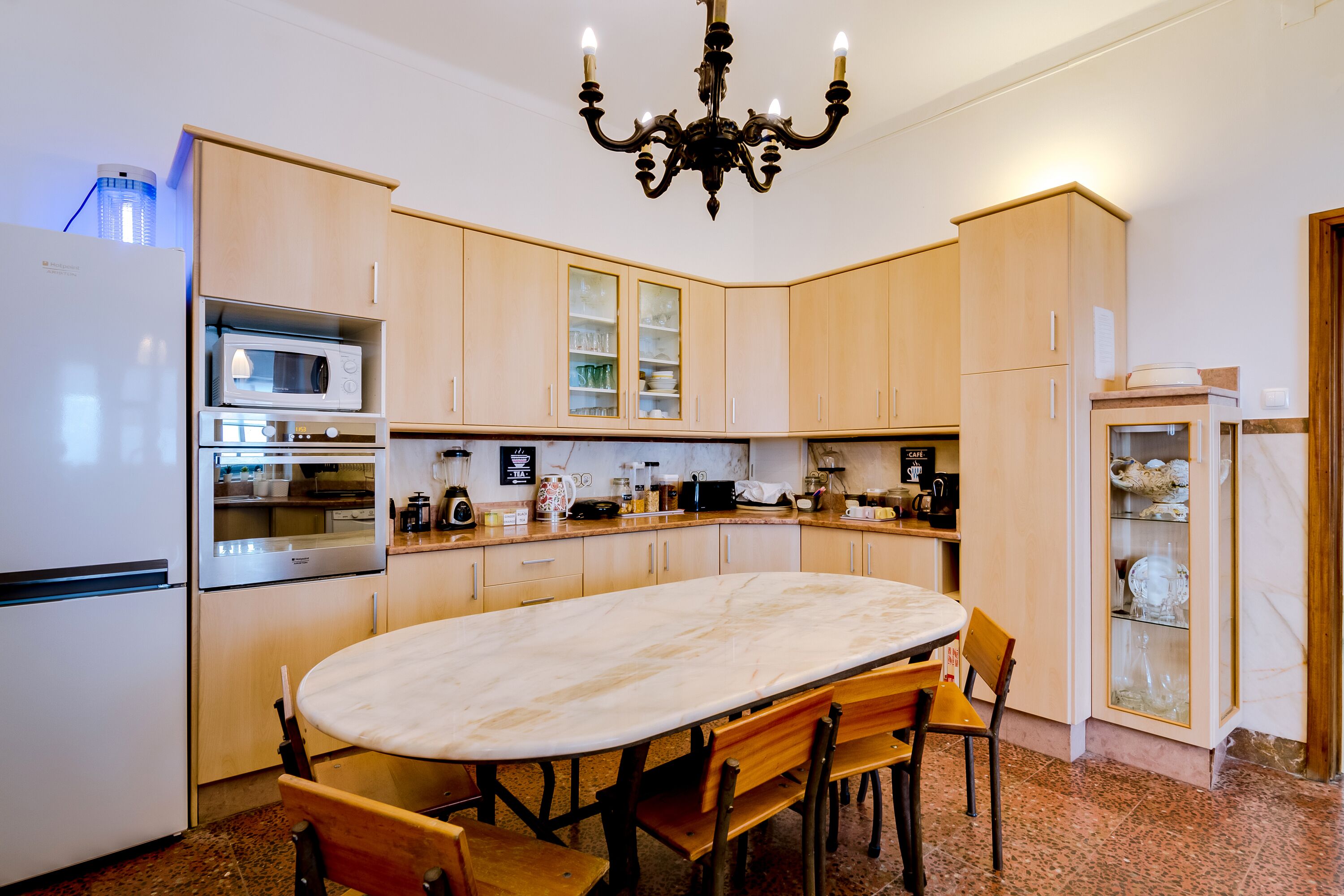 A modern kitchen with a marble table, wooden cabinets, a built-in microwave, and a chandelier.