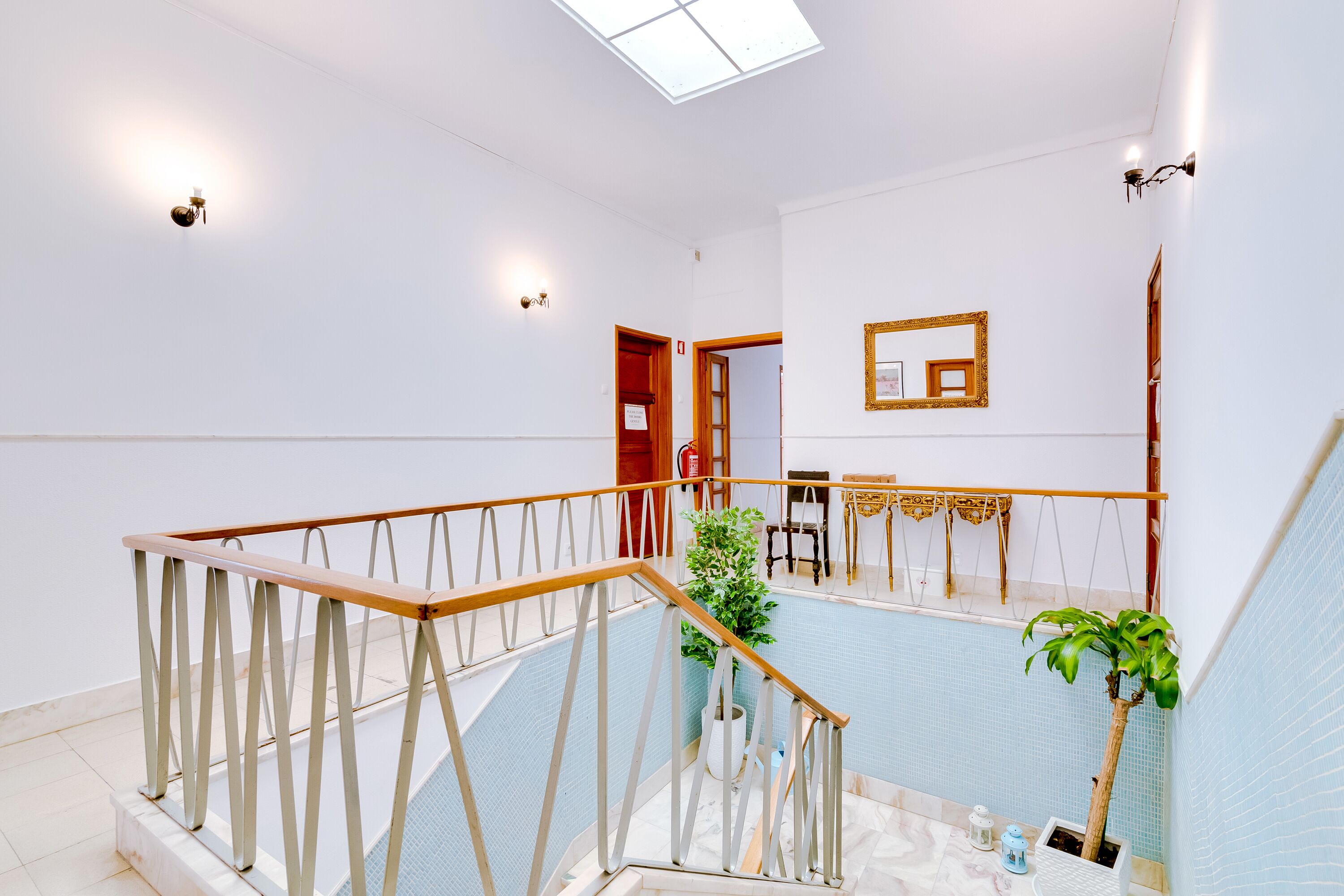 Un escalier avec une rampe en bois et des balustrades blanches, menant à une pièce dont un mur est recouvert de carreaux bleus et qui possède une porte en bois.