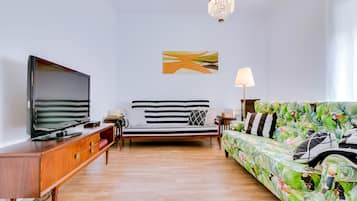 A modern living room with a flat-screen TV, a striped sofa, a patterned sofa, a wooden cabinet, and a chandelier.