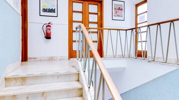 Eine Treppe führt zu einem Poolbereich, an der Wand hängt ein Feuerlöscher, es gibt Holztüren und ein gerahmtes Bild.