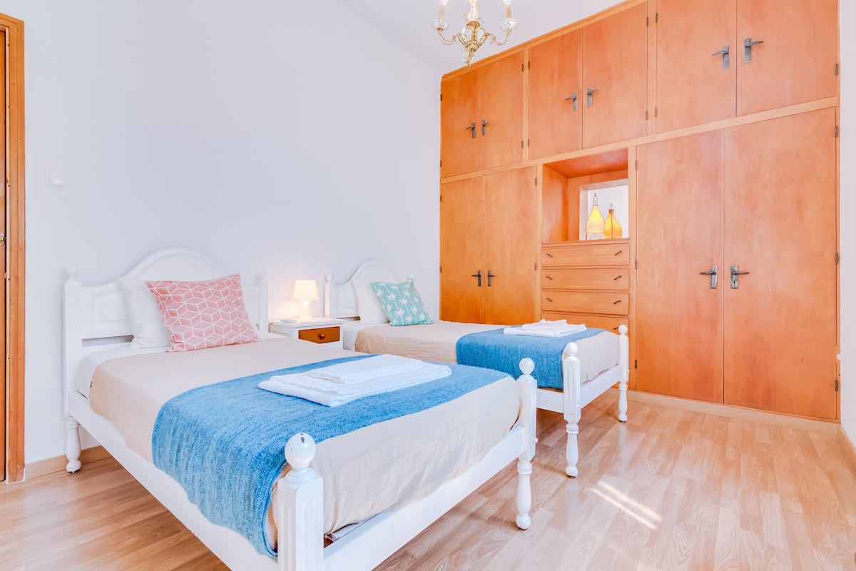 A bedroom with two beds, wooden wardrobe, and a nightstand with a lamp.