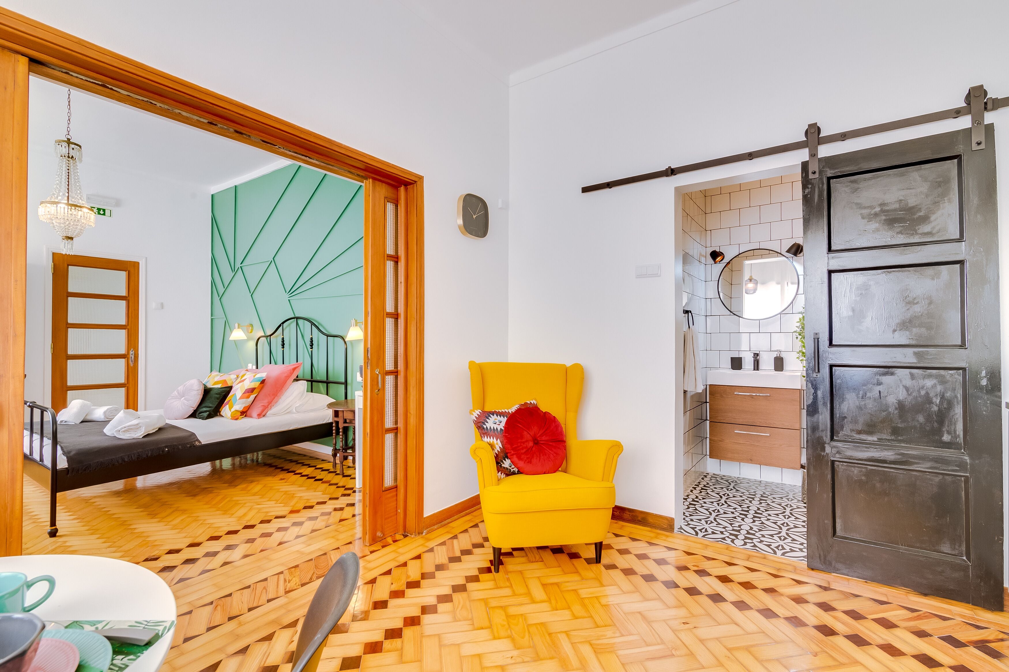 A room with a bed, a yellow armchair, a wooden floor, a sliding door, and a mirror on the wall.