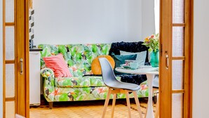 A room with a wooden floor, a green sofa with colorful cushions, a white table with a vase, and a wooden door. - À da Avó - The Guesthouse (Faro)