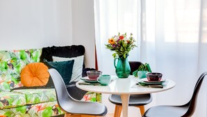 A dining area with a round table, two chairs, a vase of flowers, and a sofa with a tropical print cushion. - À da Avó - The Guesthouse (Faro)