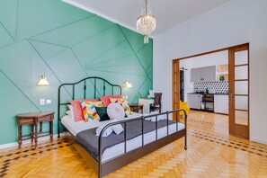 Une chambre moderne avec un mur de couleur turquoise orné d’un motif géométrique, un parquet en bois disposé en chevrons, un cadre de lit en métal et un lustre.